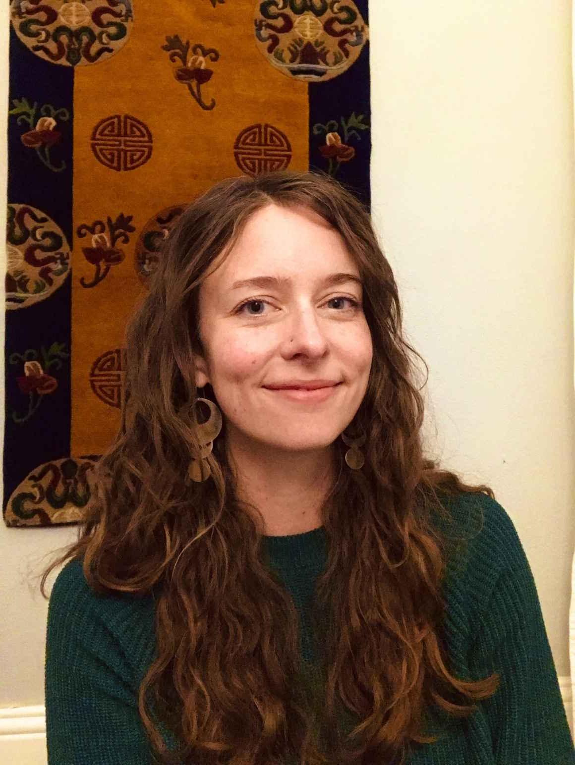凯特Falkenhart, 科罗拉多州ACLU的运营经理, 微笑, 在浅色的墙上挂着一幅棕黑相间的挂毯